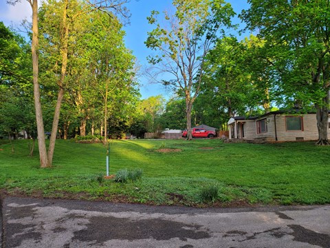 a yard with a house and a red car in the background