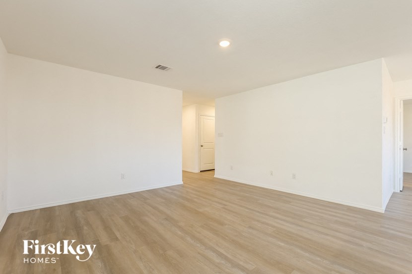 A spacious room with wooden flooring and white walls, with a door in the background.