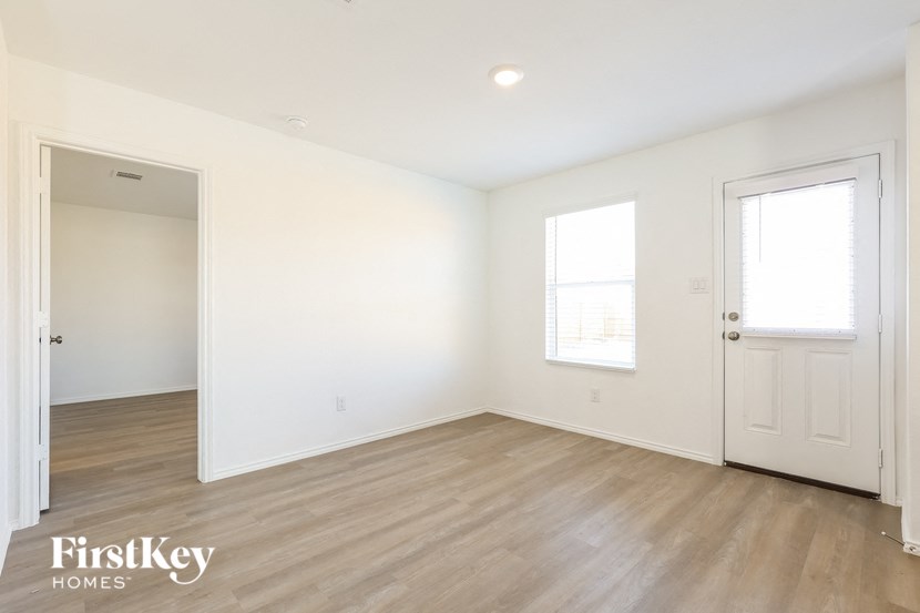 A room with wooden floors and white walls, with a door on the left and a window on the right.