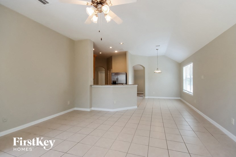 an empty living room with a kitchen and a ceiling fan