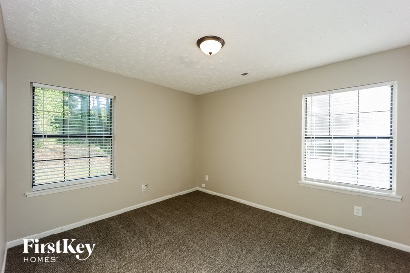 an empty bedroom with two windows and a carpeted floor