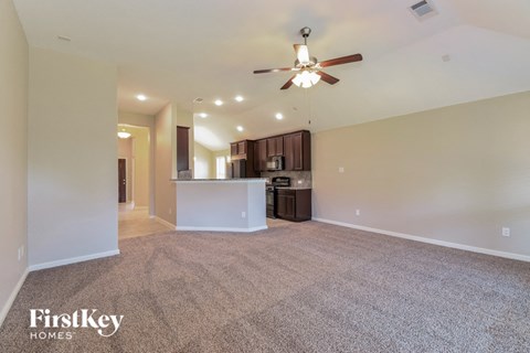 an empty living room with a ceiling fan and a kitchen