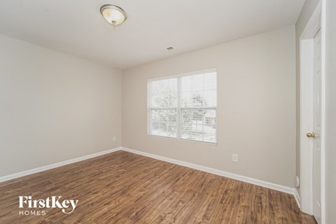 A room with wooden flooring and a window showing a view of trees and buildings outside.