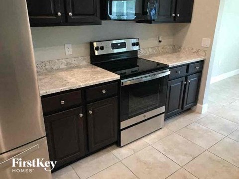 A kitchen with black cabinets and a stainless steel refrigerator.
