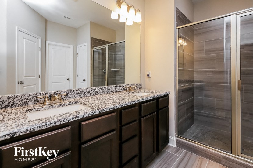 the master bathroom has a large shower and granite counter tops and dark wood cabinets