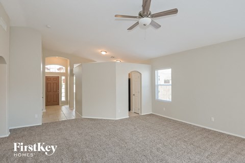the living room and entryway of an empty house with a ceiling fan
