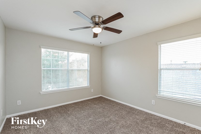 an empty bedroom with a ceiling fan and two windows
