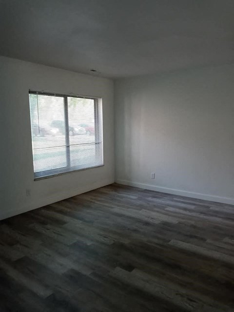 an empty living room with a window and wooden floors