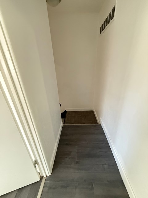 A long hallway with a white door on the left and a vent on the wall.