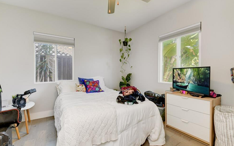 A bedroom with a bed, a desk with a chair, and a window with a view of a tree.