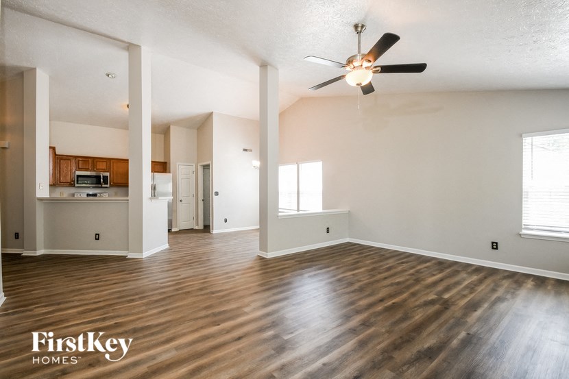 an empty living room with a ceiling fan and a kitchen