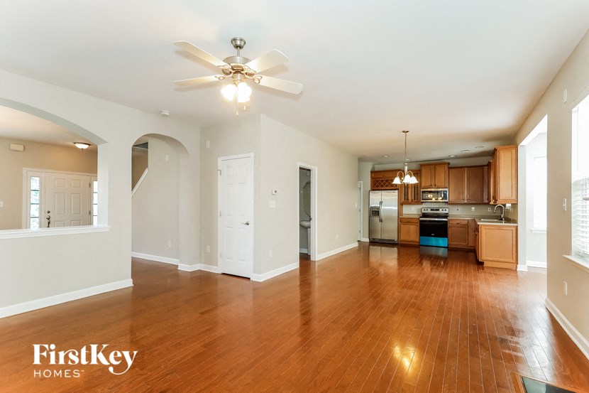 an empty living room and kitchen with wood flooring and a ceiling fan