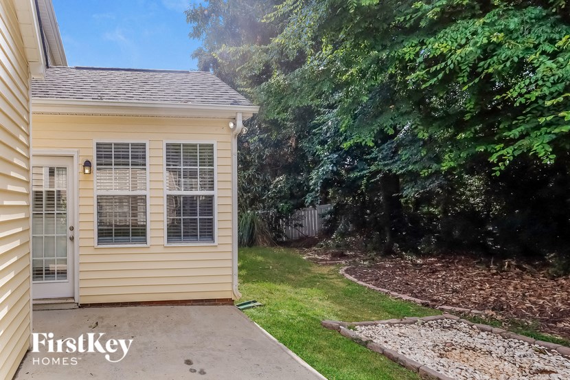 a small yellow house with a driveway and some trees