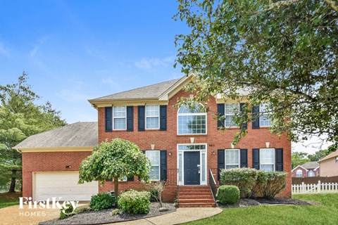 a brick house with a white fence and a tree