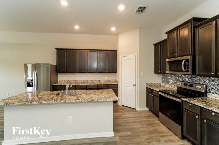 A kitchen with granite countertops and dark brown cabinets.