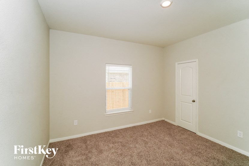A room with a carpeted floor, a window with blinds, and a door.