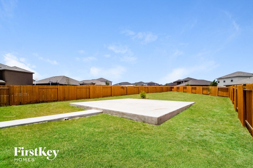 A backyard with a wooden fence and a concrete slab in the middle.