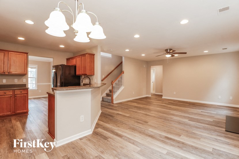 an empty living room with a kitchen and a ceiling fan