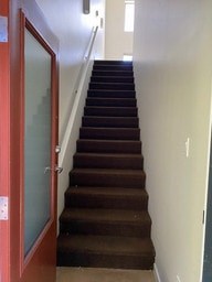 A brown carpeted staircase with a red door on the left.