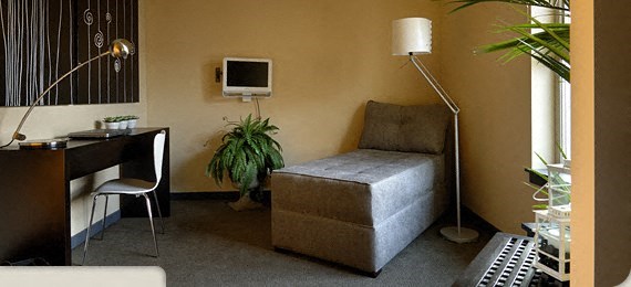 A room with a bed, desk, chair, and a plant.