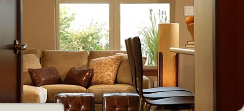 A brown couch with pillows and a chair in front of a window.