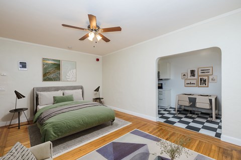 A bedroom with a bed, a chair, a ceiling fan and a checkered floor.