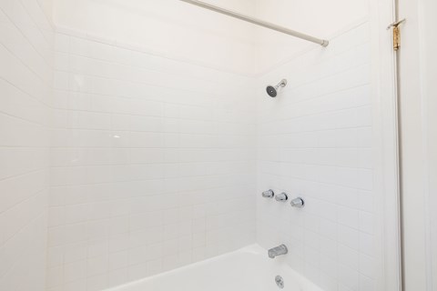 A white tiled shower with a white tub and a white shower head.