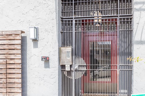 A red car is behind a metal gate with the number 421 on it.