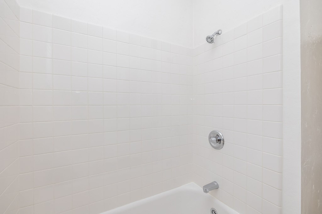 a white tiled bathroom with a tub and a shower