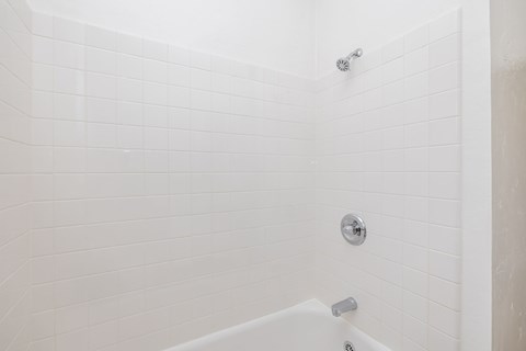 A white tiled shower with a white tub and a shower head.