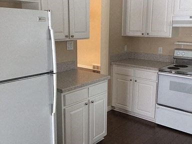 A white refrigerator stands in a kitchen with white cabinets.