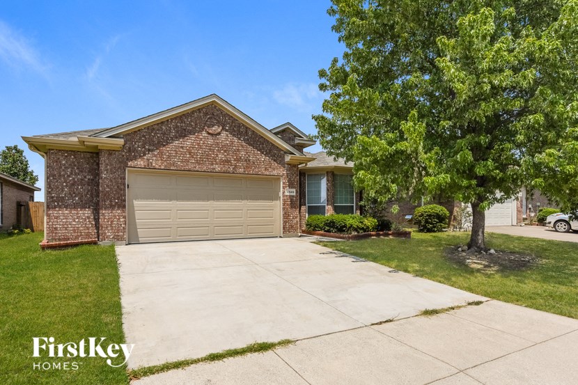 A brick house with a garage door and a tree in front.