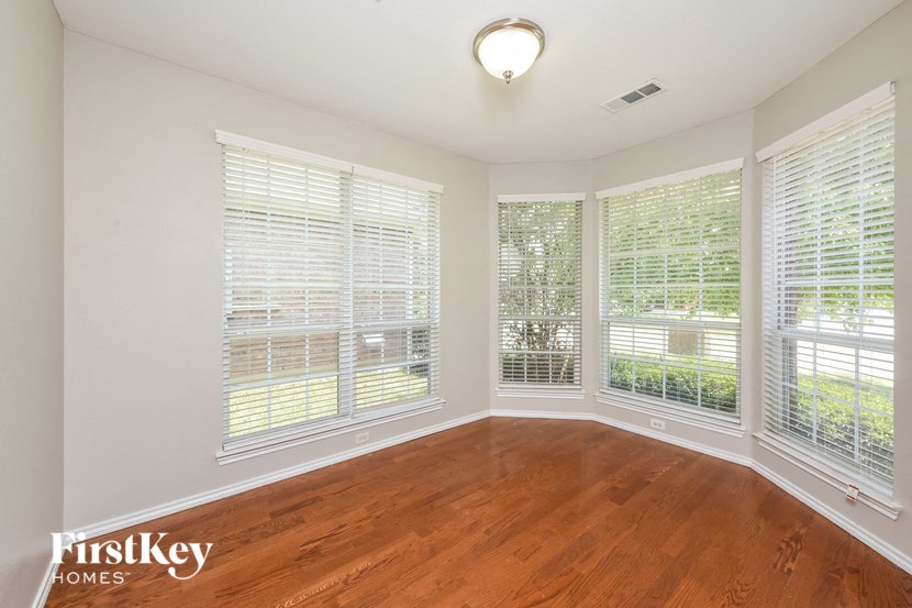 A room with wooden floors and white walls, with a window covered in white blinds.