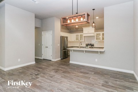 an empty living room with a kitchen and a chandelier