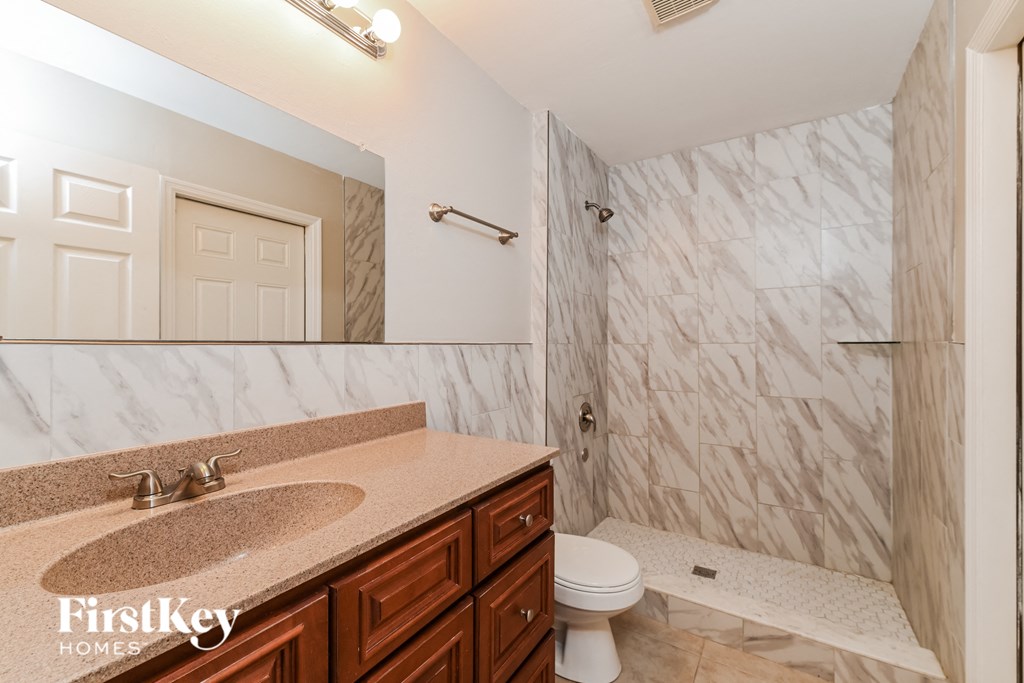 A bathroom with a marble tile shower and a sink with a granite countertop.