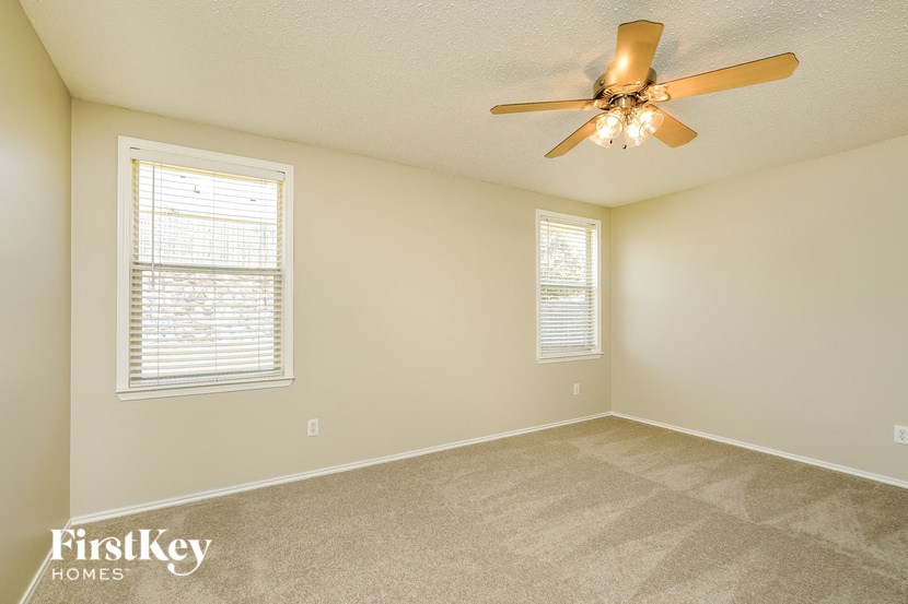 an empty room with a ceiling fan and two windows