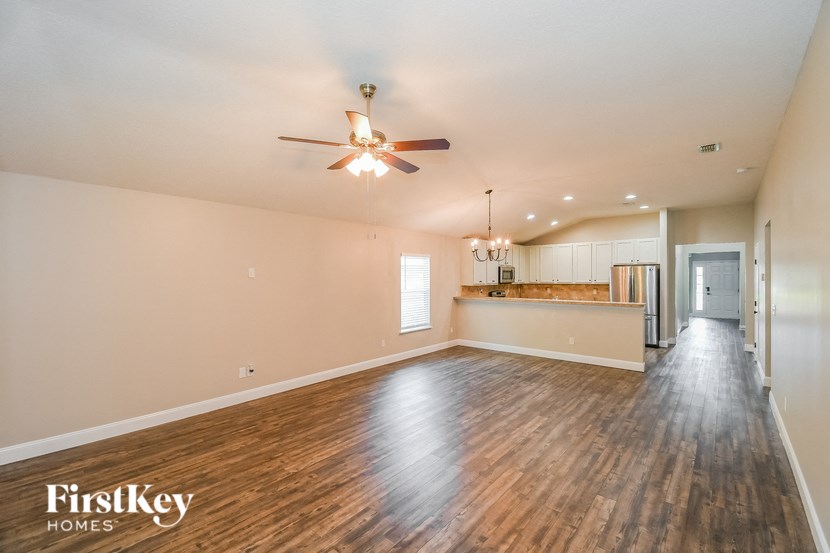 an empty living room with a ceiling fan and a kitchen