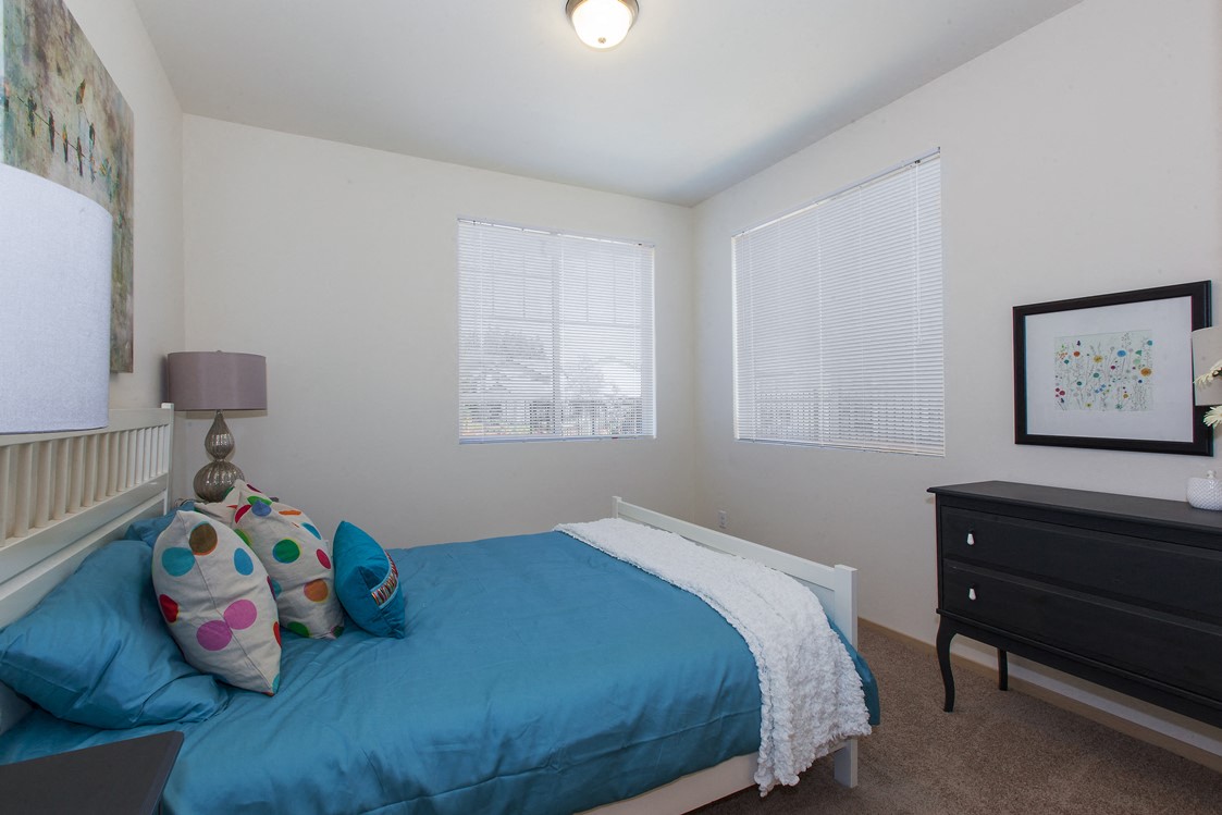 a bedroom with a bed and a dresser and two windows
