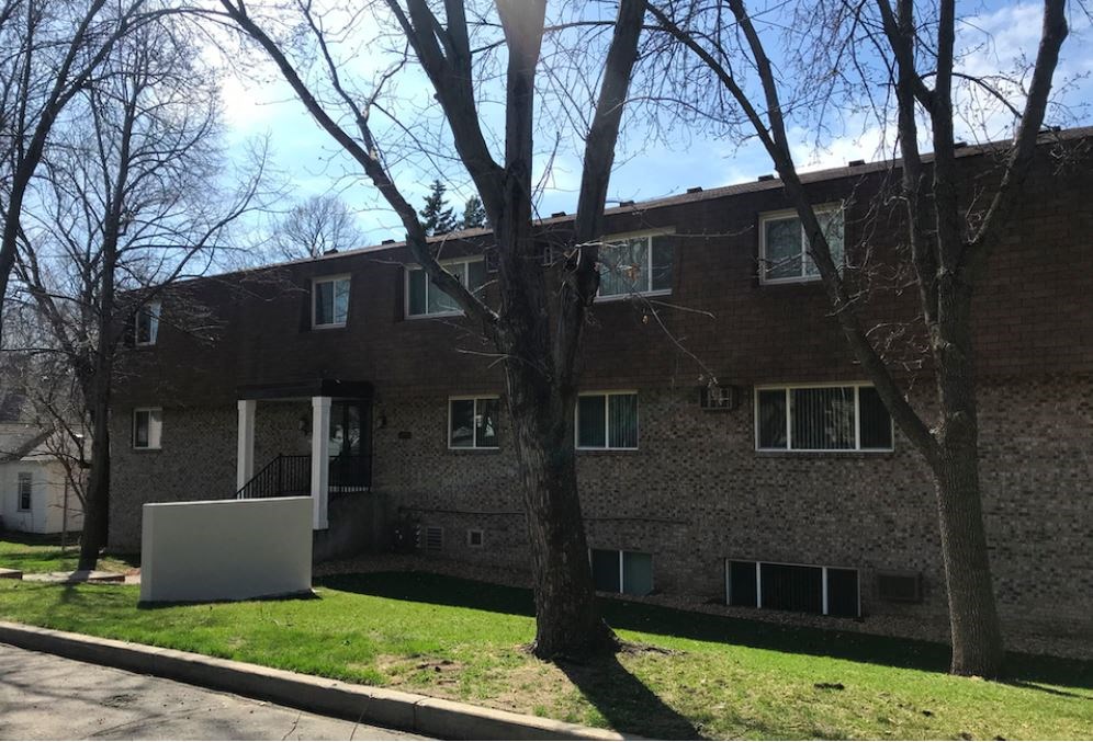 a brick building with a lawn and trees in front of it