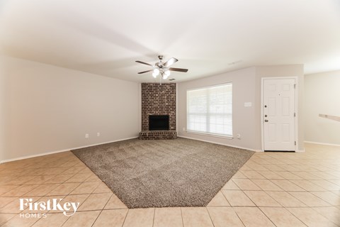 A spacious living room with a fireplace and a rug in the center.