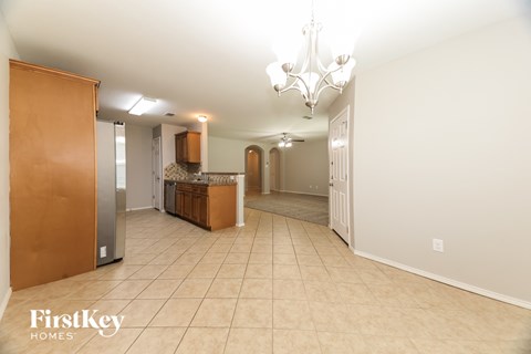 A spacious room with a chandelier and a kitchen area in the background.