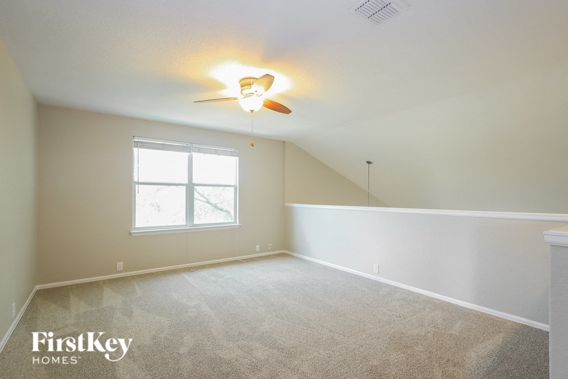 A room with a carpet floor, a ceiling fan, and a window.
