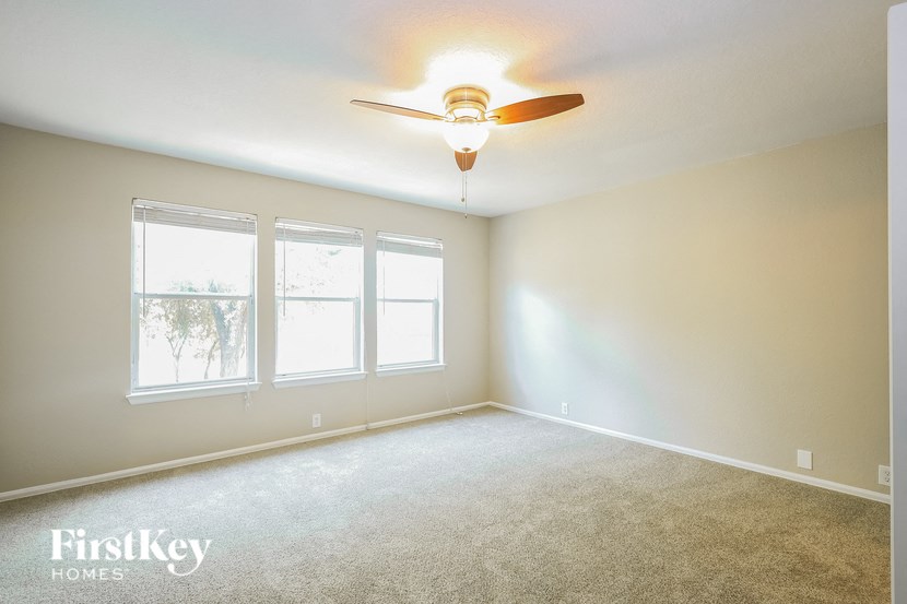 A room with a carpet floor, a ceiling fan, and three windows.