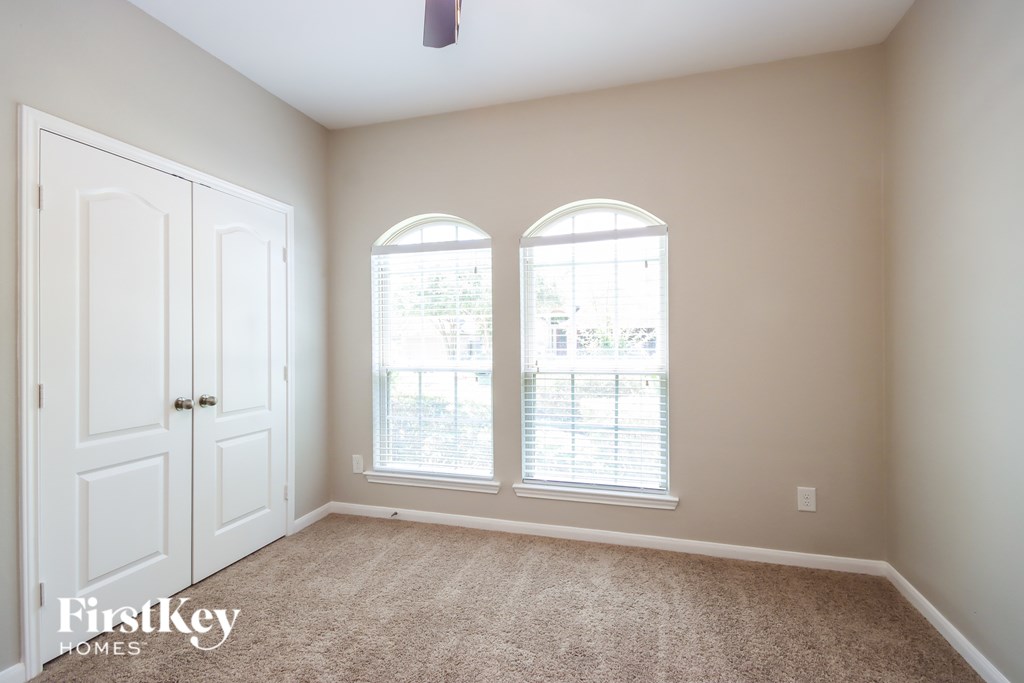 A room with a carpeted floor, two windows, and a door.