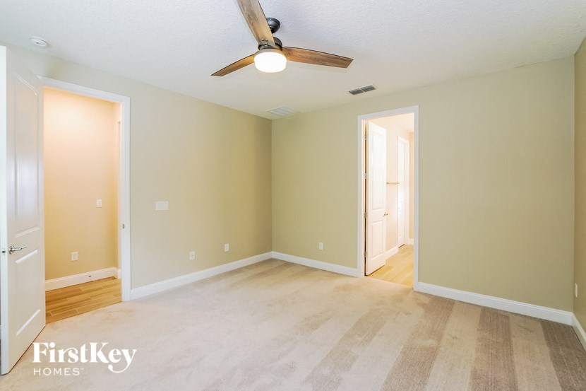 A room with a ceiling fan and light fixture, and a doorway leading to another room.