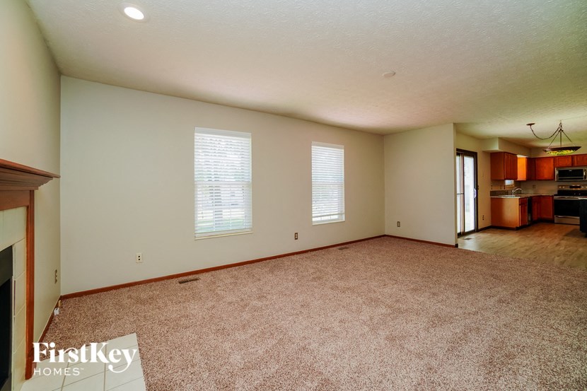 an empty living room with a kitchen in the background