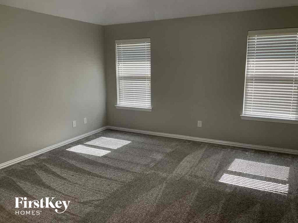 A room with a grey carpet and two windows with blinds.