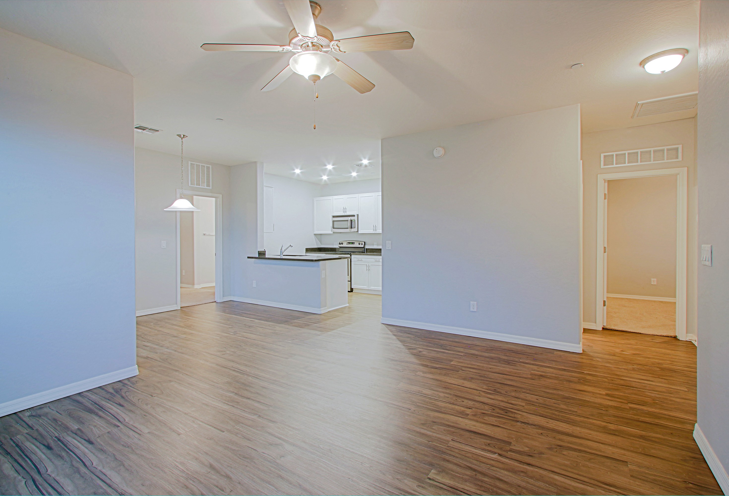 an empty living room with a ceiling fan and a kitchen