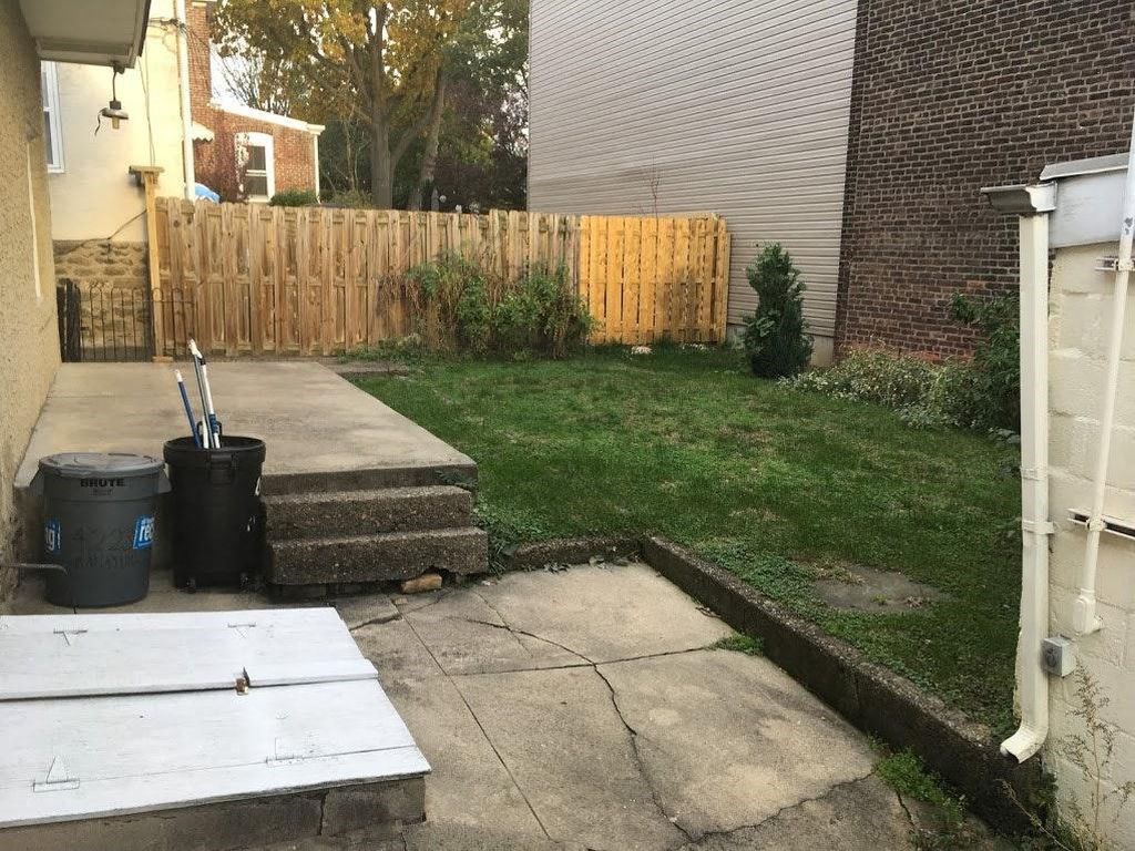 A backyard with a wooden fence and a trash can.