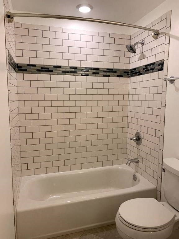 a white tiled bathroom with a toilet and a bath tub